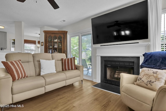 5109 Gate Post Ln, Wilmington, NC 28412 - living area featuring ceiling fan, wood finished floors, a fireplace with raised hearth, a textured ceiling, and healthy amount of natural light