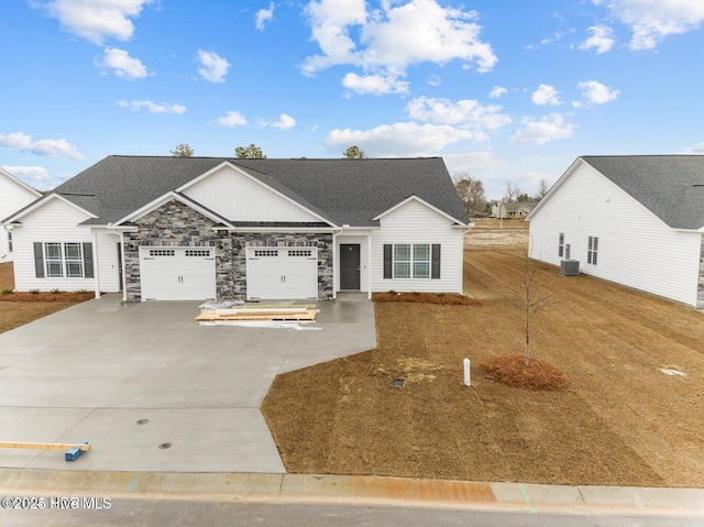 view of front of property with driveway, central air condition unit, an attached garage, stone siding, and a shingled roof