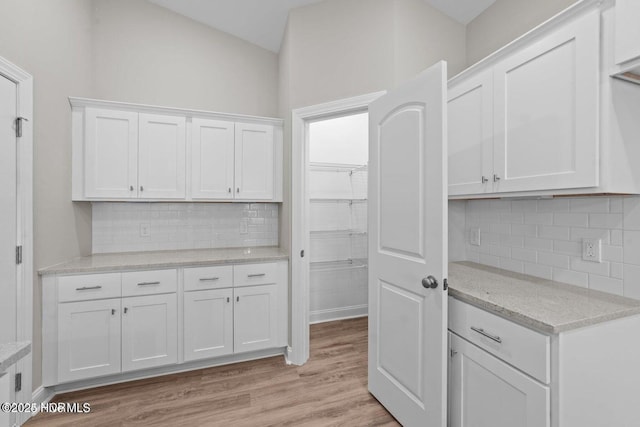 kitchen featuring white cabinets, backsplash, light wood-style flooring, light stone countertops, and lofted ceiling