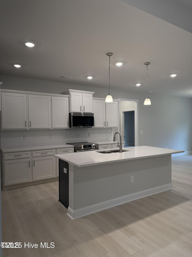 kitchen with appliances with stainless steel finishes, a sink, recessed lighting, a center island with sink, and hanging light fixtures