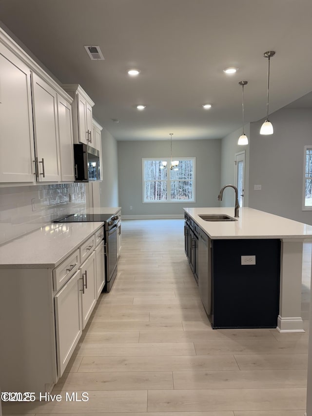 kitchen with a sink, stainless steel microwave, black electric range oven, baseboards, and light wood-type flooring
