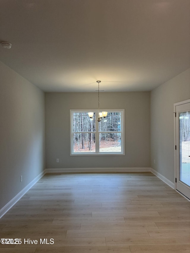 unfurnished dining area featuring a chandelier, light wood-style flooring, and baseboards