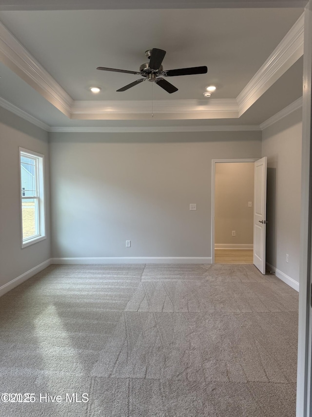 spare room with a tray ceiling, ornamental molding, carpet flooring, a ceiling fan, and baseboards