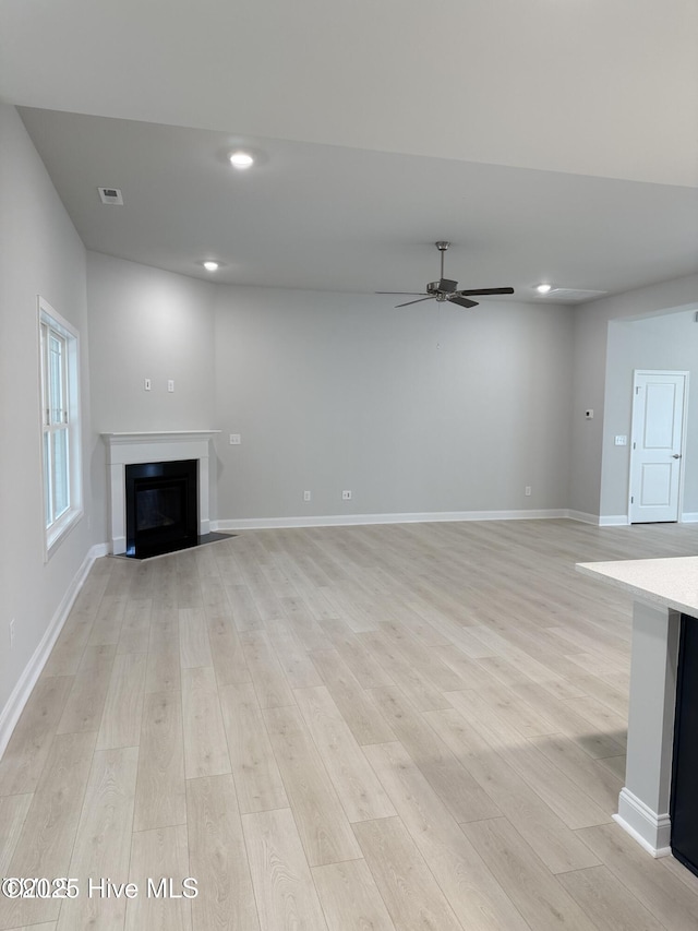 unfurnished living room featuring a ceiling fan, light wood finished floors, a glass covered fireplace, recessed lighting, and baseboards