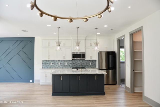 120 Fairview Rd, Leland, NC 28451 - kitchen featuring appliances with stainless steel finishes, white cabinetry, decorative backsplash, light wood-style floors, and an island with sink