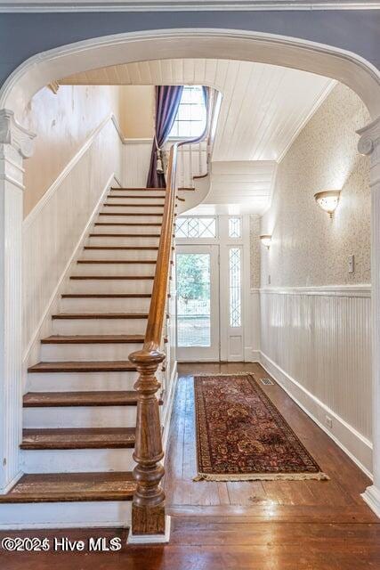 staircase featuring arched walkways, hardwood / wood-style flooring, a wainscoted wall, and ornamental molding