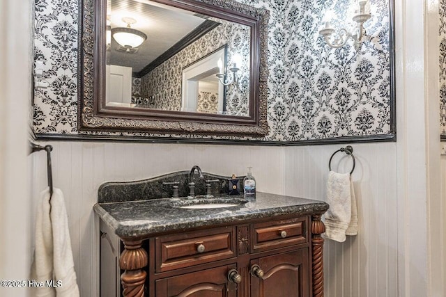 bathroom featuring wallpapered walls, wainscoting, vanity, and crown molding