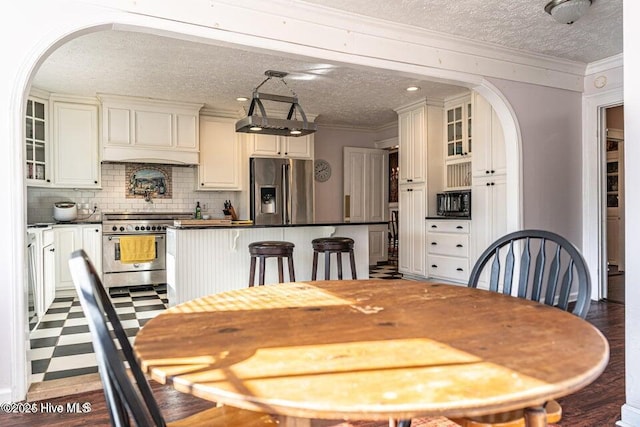 dining space featuring arched walkways, a textured ceiling, ornamental molding, and dark wood finished floors