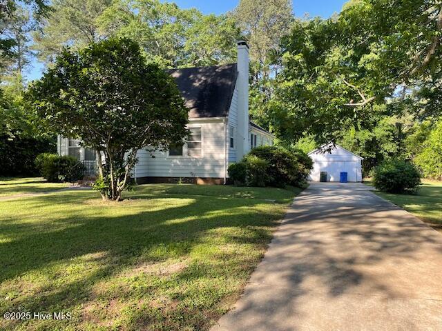 view of front of property featuring a detached garage, a front lawn, and a chimney