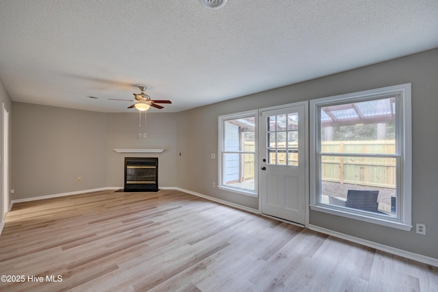 4941 Marlin Ct, Wilmington, NC 28403 - unfurnished living room featuring a textured ceiling, light wood finished floors, ceiling fan, a fireplace with flush hearth, and baseboards