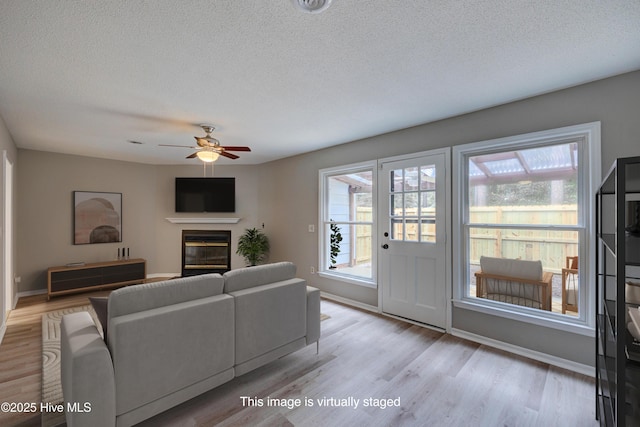 4941 Marlin Ct, Wilmington, NC 28403 - living room featuring a textured ceiling, wood finished floors, baseboards, a ceiling fan, and a glass covered fireplace