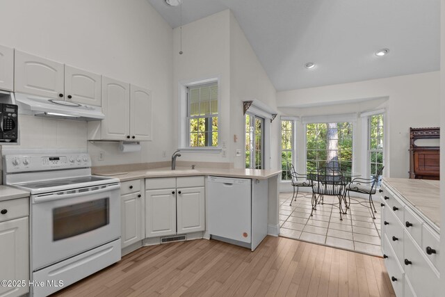 3665 Willow Lake Dr SE, Southport, NC 28461 - kitchen with white appliances, a sink, under cabinet range hood, high vaulted ceiling, and white cabinetry