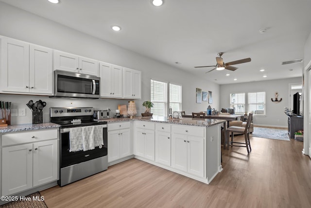 5021 Northstar Dr, Leland, NC 28451 - kitchen with stainless steel appliances, a peninsula, ceiling fan, light wood-type flooring, and white cabinets