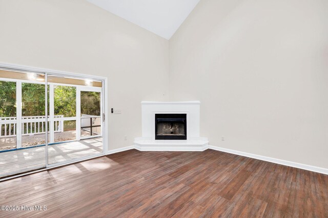 562 Anchor Way, Kure Beach, NC 28449 - unfurnished living room with wood finished floors, baseboards, high vaulted ceiling, and a fireplace with raised hearth