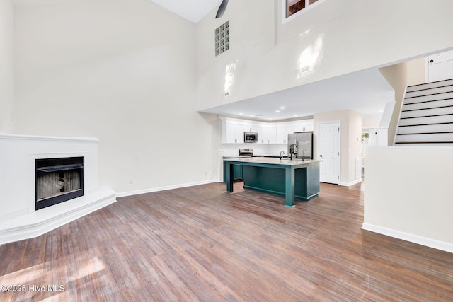 562 Anchor Way, Kure Beach, NC 28449 - unfurnished living room featuring baseboards, stairs, wood finished floors, high vaulted ceiling, and a fireplace with raised hearth