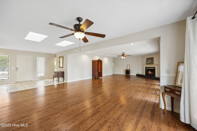 7 Prichard Ln, Pinehurst, NC 28374 - unfurnished living room featuring a lit fireplace, wood finished floors, a ceiling fan, a skylight, and recessed lighting