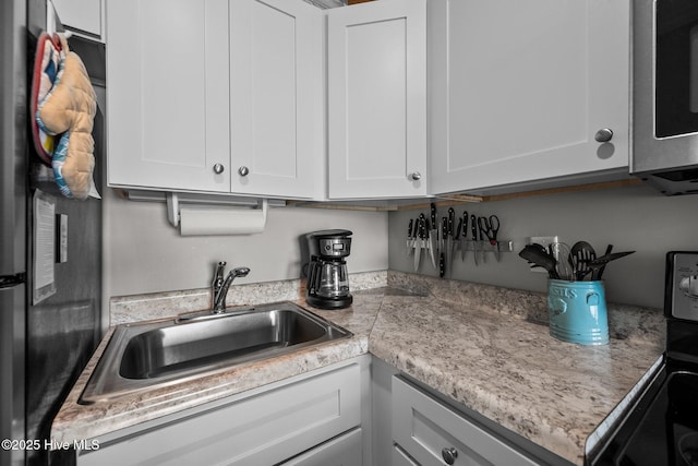 kitchen with freestanding refrigerator, light countertops, white cabinetry, a sink, and stainless steel microwave