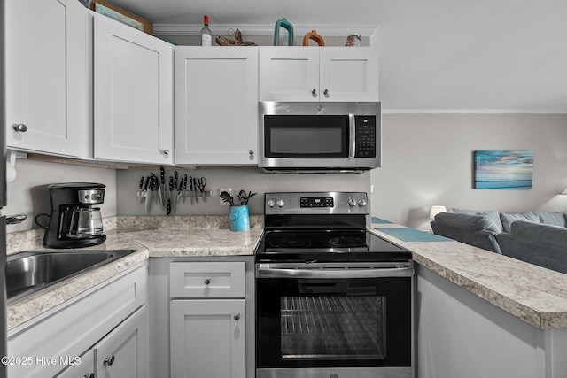 kitchen featuring stainless steel appliances, light countertops, crown molding, white cabinetry, and open floor plan