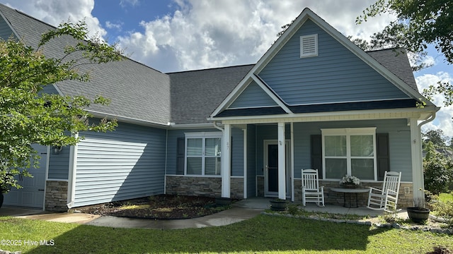 87 Strut Way, Rocky Point, NC 28457 - view of front facade with covered porch, stone siding, an attached garage, a front yard, and a shingled roof
