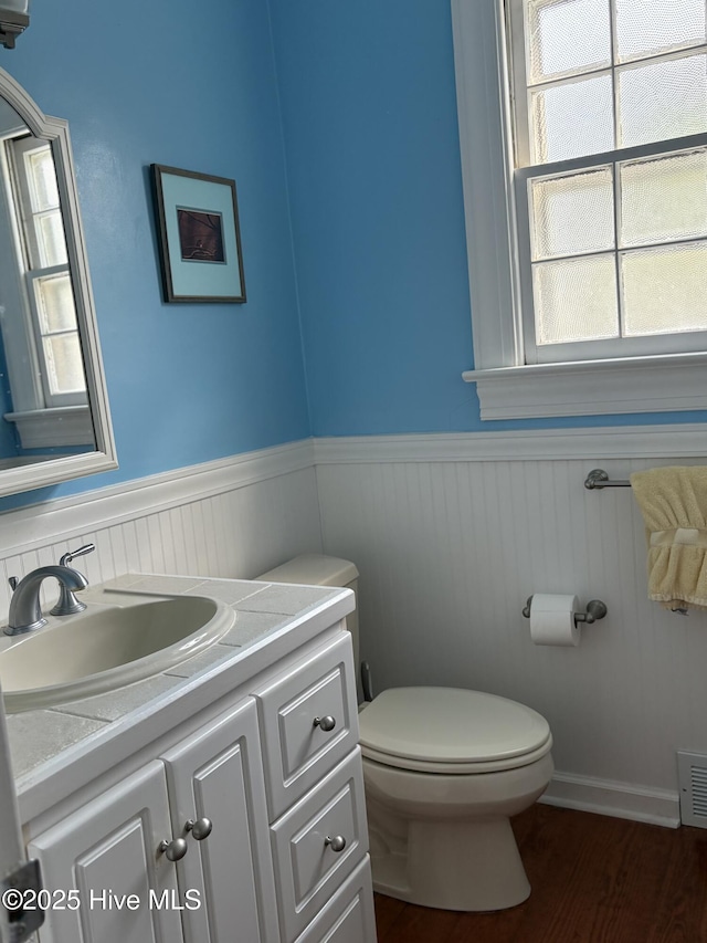 215 W Queen St, Edenton, NC 27932 - half bathroom with a wainscoted wall, toilet, healthy amount of natural light, vanity, and wood finished floors