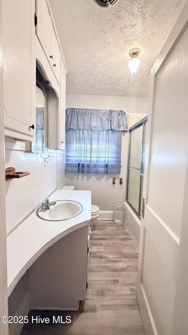 308 Terry St, Hamlet, NC 28345 - bathroom featuring vanity, wood finished floors, toilet, baseboards, and bath / shower combo with glass door