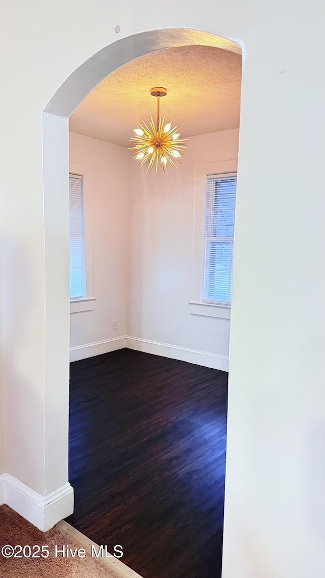 308 Terry St, Hamlet, NC 28345 - empty room featuring arched walkways, baseboards, a chandelier, and dark wood-style flooring