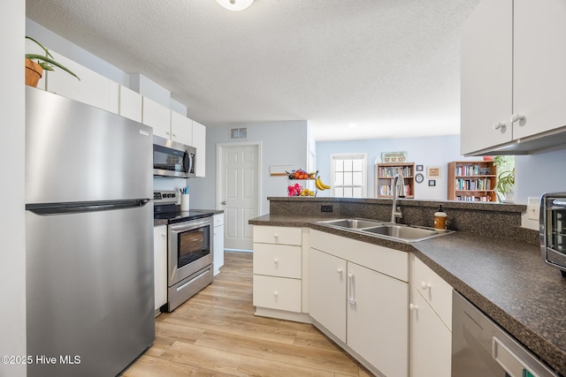 130 Woodgreen Ln, Aberdeen, NC 28315 - kitchen featuring stainless steel appliances, a sink, light wood-style flooring, dark countertops, and a textured ceiling