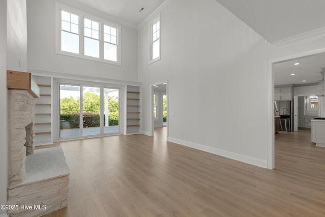 1401 Regatta Dr, Wilmington, NC 28405 - unfurnished living room with crown molding, baseboards, light wood-style flooring, healthy amount of natural light, and a stone fireplace