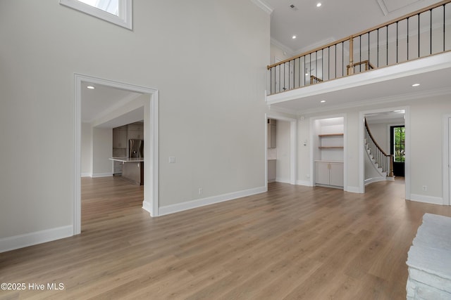 1401 Regatta Dr, Wilmington, NC 28405 - unfurnished living room featuring a towering ceiling, crown molding, stairs, baseboards, and light wood-type flooring