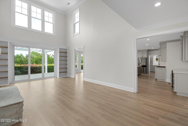 1401 Regatta Dr, Wilmington, NC 28405 - unfurnished living room featuring ornamental molding, light wood-style flooring, baseboards, recessed lighting, and a towering ceiling