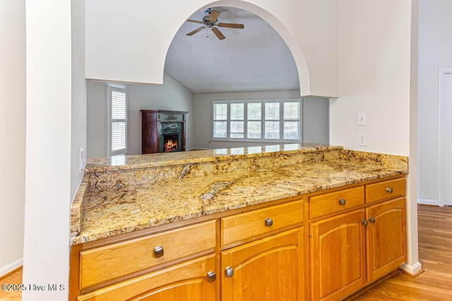 129 Shagbark Ct, West End, NC 27376 - kitchen featuring ceiling fan, light stone countertops, lofted ceiling, a lit fireplace, and light wood-style flooring