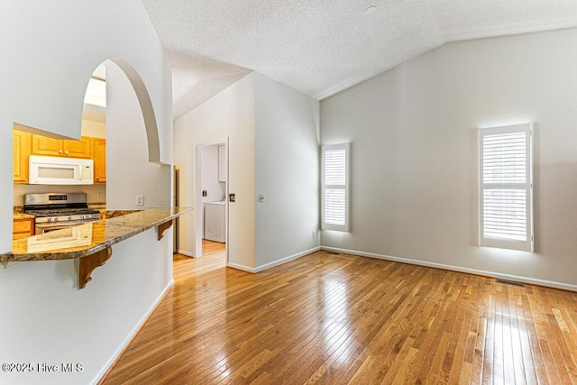 129 Shagbark Ct, West End, NC 27376 - kitchen featuring stainless steel range with gas stovetop, white microwave, vaulted ceiling, a kitchen breakfast bar, and light wood-type flooring