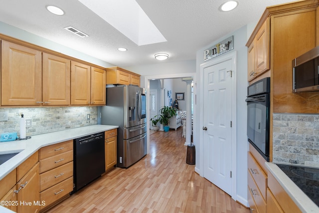4 Golf Crest Ct, Carolina Shores, NC 28467 - kitchen featuring black appliances, a skylight, light wood-type flooring, decorative backsplash, and light countertops