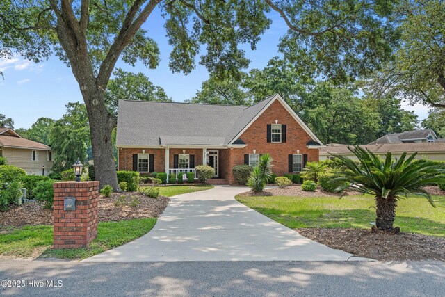 550 Sunset Lakes Blvd SW, Sunset Beach, NC 28468 - traditional-style home featuring brick siding, covered porch, a shingled roof, and driveway