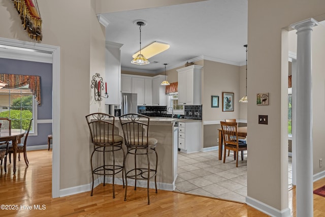 550 Sunset Lakes Blvd SW, Sunset Beach, NC 28468 - kitchen featuring a peninsula, white cabinetry, a breakfast bar, tasteful backsplash, and light wood-type flooring