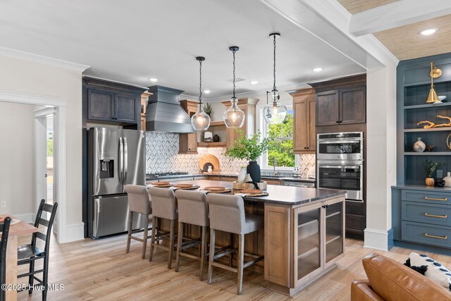 412 Keziah St, Oak Island, NC 28465 - kitchen with appliances with stainless steel finishes, custom exhaust hood, a kitchen breakfast bar, a center island, and light wood finished floors
