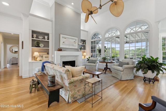 8300 Fazio Dr, Wilmington, NC 28411 - living area featuring crown molding, built in shelves, a premium fireplace, a towering ceiling, and light wood finished floors