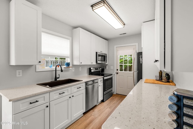 7321 Haskell Ct, Wilmington, NC 28411 - kitchen featuring stainless steel appliances, a sink, white cabinetry, light wood-style floors, and light stone counters