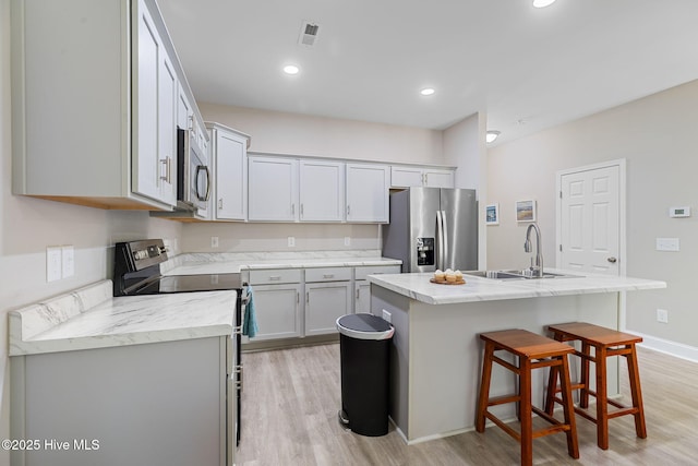 210 N Stingray Ln, Sneads Ferry, NC 28460 - kitchen with appliances with stainless steel finishes, light wood-type flooring, a sink, a breakfast bar, and a kitchen island with sink