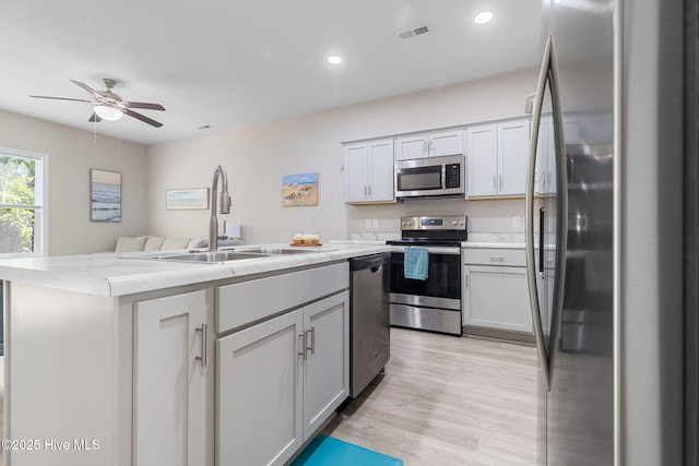 210 N Stingray Ln, Sneads Ferry, NC 28460 - kitchen featuring appliances with stainless steel finishes, a sink, a center island with sink, light wood finished floors, and ceiling fan
