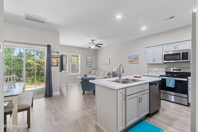 210 N Stingray Ln, Sneads Ferry, NC 28460 - kitchen featuring appliances with stainless steel finishes, a sink, light wood-style flooring, ceiling fan, and an island with sink