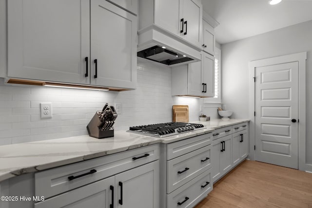 3625 Mason Port Dr, Wilmington, NC 28409 - kitchen featuring stainless steel gas cooktop, decorative backsplash, light stone countertops, light wood finished floors, and white cabinets
