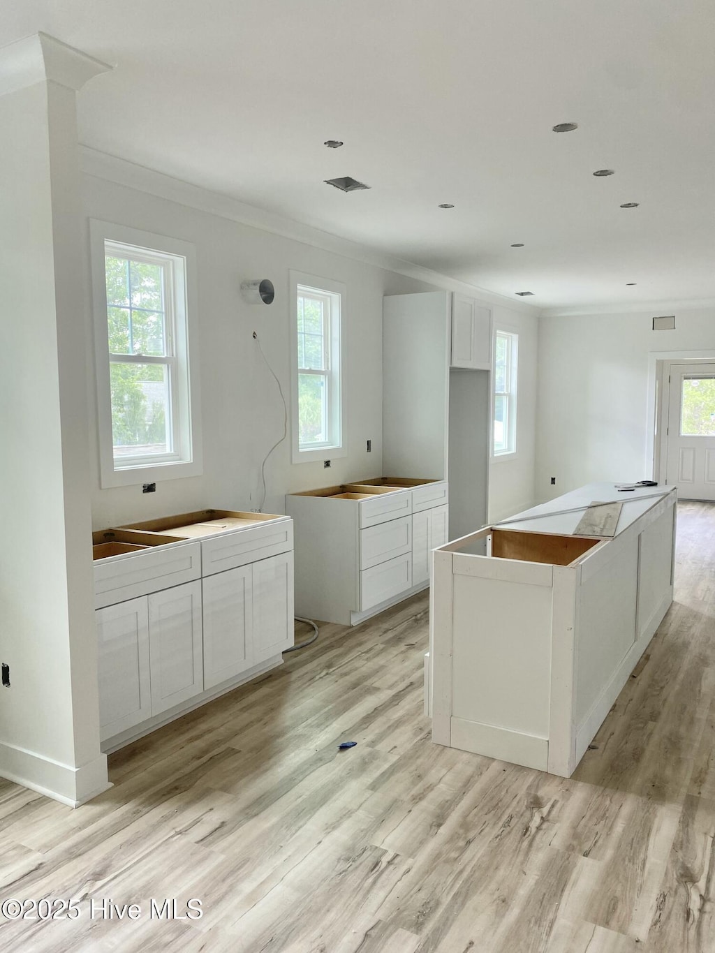 231 NE 77th St, Oak Island, NC 28465 - kitchen with light wood-type flooring, plenty of natural light, ornamental molding, a kitchen island, and white cabinets