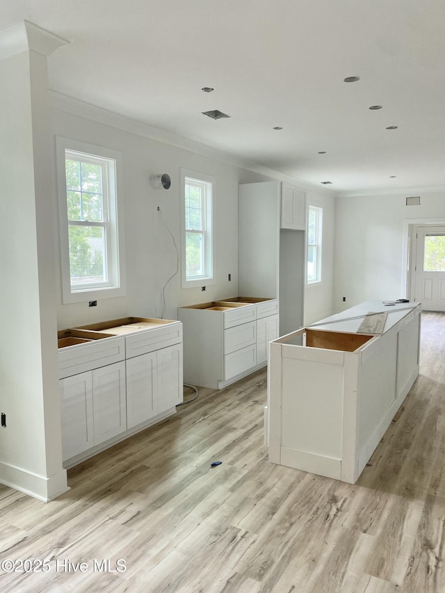 231 NE 77th St, Oak Island, NC 28465 - kitchen with light wood-type flooring, plenty of natural light, ornamental molding, a kitchen island, and white cabinets