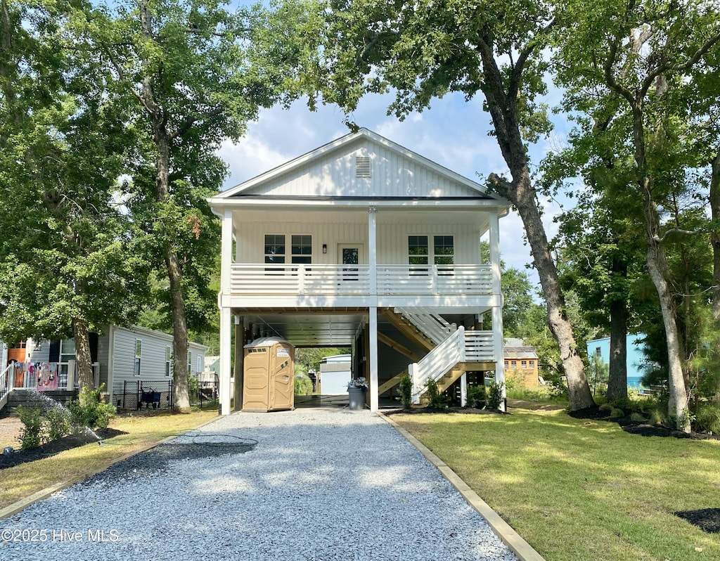 231 NE 77th St, Oak Island, NC 28465 - coastal inspired home featuring covered porch, driveway, a carport, stairway, and a front lawn