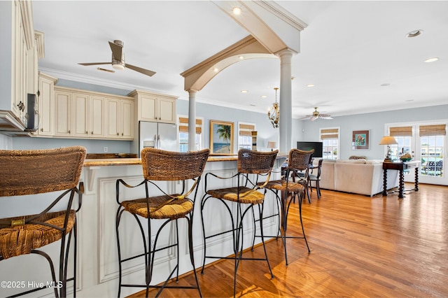 1510 N Shore Dr, Sunset Beach, NC 28468 - kitchen featuring cream cabinetry, ceiling fan, fridge with ice dispenser, decorative columns, and a kitchen bar