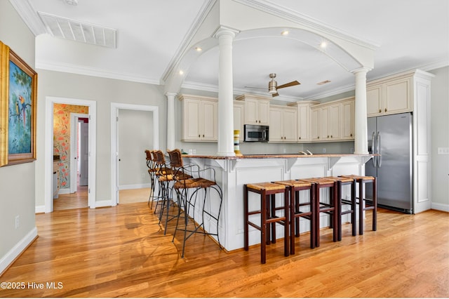 1510 N Shore Dr, Sunset Beach, NC 28468 - kitchen featuring appliances with stainless steel finishes, decorative columns, a kitchen bar, light wood finished floors, and crown molding
