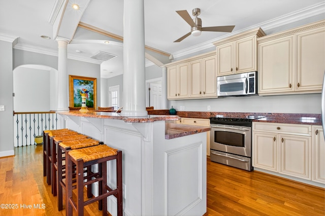 1510 N Shore Dr, Sunset Beach, NC 28468 - kitchen with stainless steel appliances, cream cabinetry, ornate columns, crown molding, and a kitchen breakfast bar