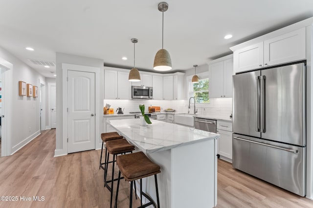 1015 E Moore St, Southport, NC 28461 - kitchen with stainless steel appliances, a kitchen island, a sink, decorative backsplash, and light wood-type flooring