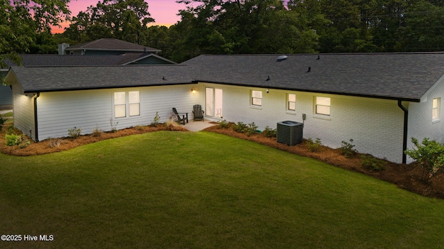 1015 E Moore St, Southport, NC 28461 - back of property at dusk with a shingled roof, a lawn, central AC unit, and brick siding